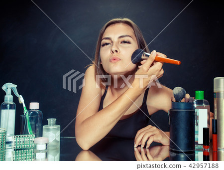 Beauty woman applying makeup. Beautiful girl looking in the mirror and applying cosmetic with a big 42957188
