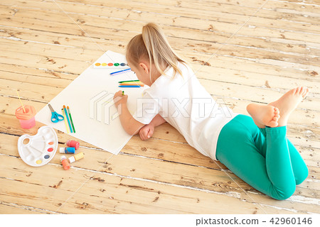 Top view of little blonde girl painting on big white paper while laying on the floor indoors Top view of little blonde girl painting on big white paper while laying on the floor indoors 42960146