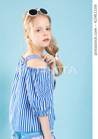 A girl in a T-shirt and shorts with glasses on her head is standing on a blue background. A girl in a T-shirt and shorts with glasses on her head is standing on a blue background. 42961109