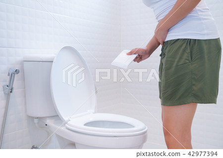 Woman holding sanitary napkins in font of toilet Woman holding sanitary napkins in font of toilet 42977394