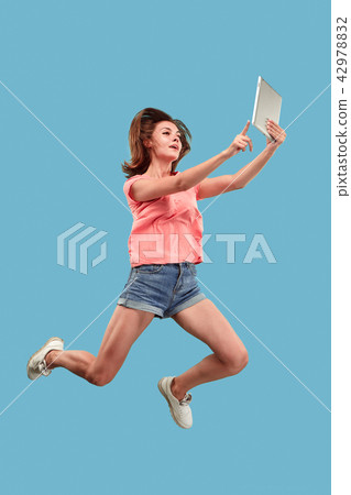 Image of young woman over blue background using laptop computer or tablet gadget while jumping. Image of young woman over blue background using laptop computer or tablet gadget while jumping. 42978832