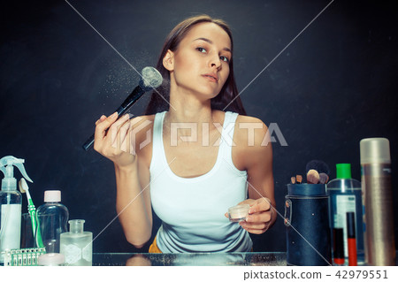 Beauty woman applying makeup. Beautiful girl looking in the mirror and applying cosmetic with a big 42979551