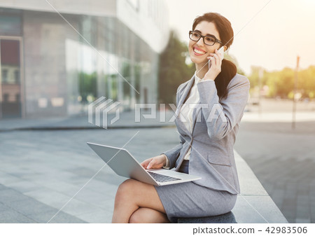 Smiling businesswoman working on laptop outdoors Smiling businesswoman working on laptop outdoors 42983506
