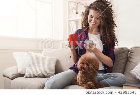 Smiling young woman with mobile and little dog at home 42983543
