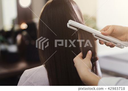 Hair straightening by a hairdresser in a professional salon, 42983718