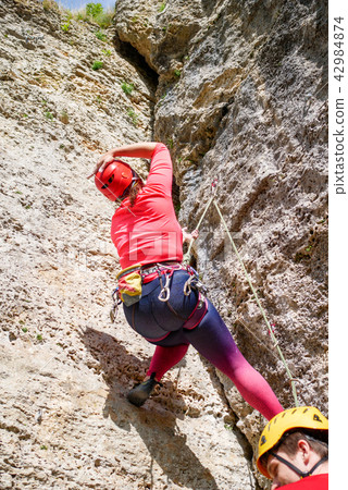 Photo from back of sporty woman in red hard hat and man climbing mountain up Photo from back of sporty woman in red hard hat and man climbing mountain up 42984874