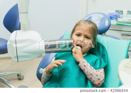 Child with a mother at a dentist's reception. The girl lies in the chair, behind her mother. The 42986934