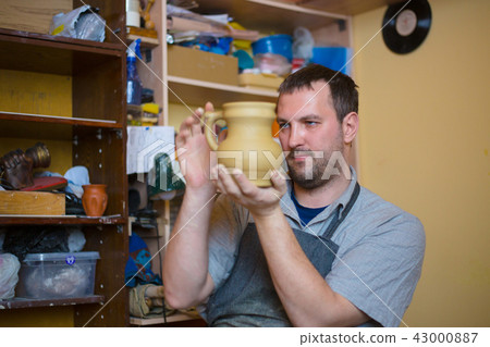 Professional male potter examining jar in pottery workshop Professional male potter examining jar in pottery workshop 43000887
