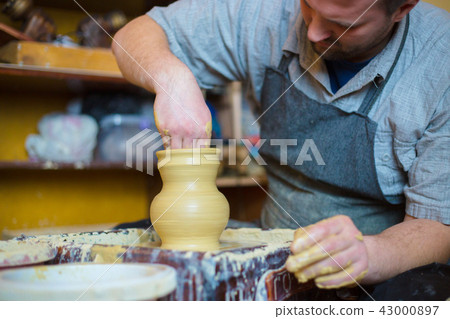 Professional male potter working with clay on potter's wheel 43000897