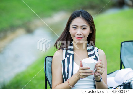 Asian girl holding a cup of coffee near the stream Asian girl holding a cup of coffee near the stream 43000925