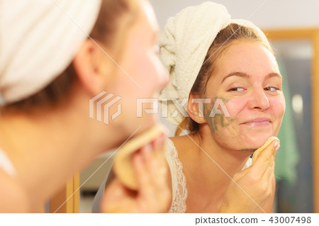 Woman removing facial clay mud mask in bathroom Woman removing facial clay mud mask in bathroom 43007498