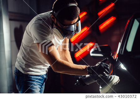 Car detailing - man with orbital polisher in auto repair shop. Selective focus. Car detailing - man with orbital polisher in auto repair shop. Selective focus. 43010372