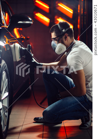 Car detailing - man with orbital polisher in auto repair shop. Selective focus. Car detailing - man with orbital polisher in auto repair shop. Selective focus. 43010671