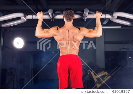 Strong young man doing pull up exercise on horizontal bar in gym Strong young man doing pull up exercise on horizontal bar in gym 43019397