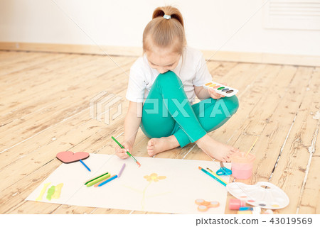 Little blonde girl paints on big white paper sitting on the floor indoors Little blonde girl paints on big white paper sitting on the floor indoors 43019569