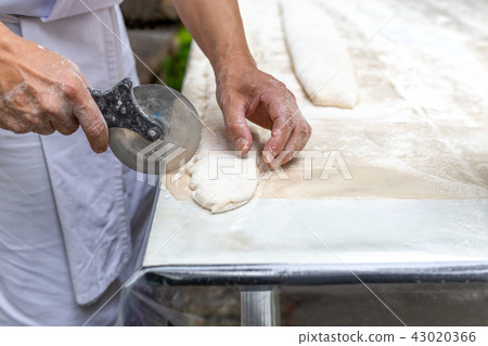Chef cutting pastry with pizza knife on table top 43020366