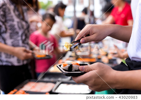 Hand picking sushi roll from food stall Hand picking sushi roll from food stall 43020983
