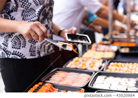 Hand picking sushi roll from food stall Hand picking sushi roll from food stall 43020984