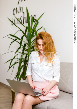 Business and training. beautiful young red haired long hair Caucasian woman uses laptop while Business and training. beautiful young red haired long hair Caucasian woman uses laptop while 43029083