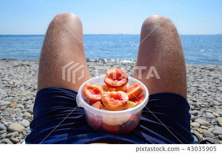 Peaches on the knees. Peeled peaches in a cup on male hairy legs. Beach vacation by the sea 43035905