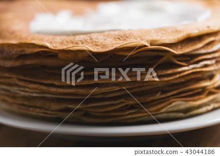 close-up of stack of fresh hot crepes or blinis with sour cream on wood table 43044186