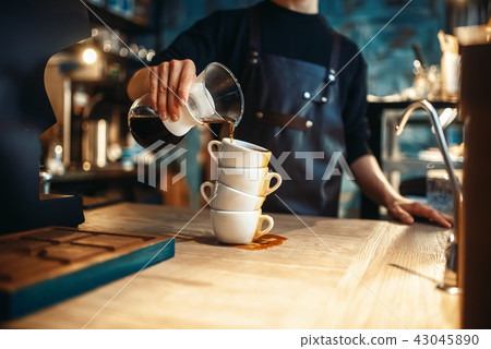 Male barista pours black coffee on a stack of cups Male barista pours black coffee on a stack of cups 43045890