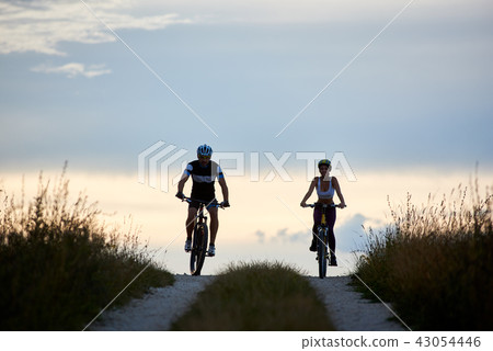 Pair of bicyclist riding bikes on country road. Fit young people in sportswear cycling downhill Pair of bicyclist riding bikes on country road. Fit young people in sportswear cycling downhill 43054446