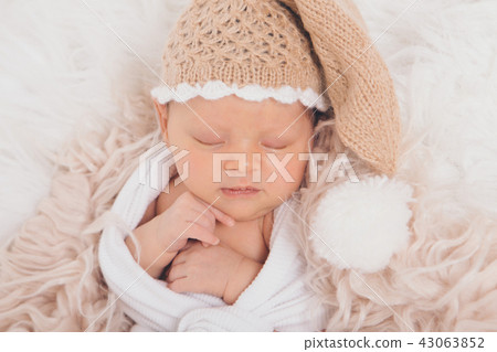 A small child in a beige knitted hat with a pompom folded his hands and sleeping A small child in a beige knitted hat with a pompom folded his hands and sleeping 43063852