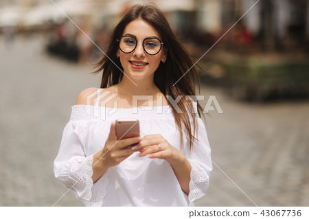 Attractive smiling young female texting on cell phone outdoors in city 43067736