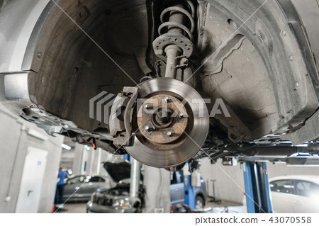 Car mechanic inspecting car wheel and repair suspension detail. Lifted automobile at repair service Car mechanic inspecting car wheel and repair suspension detail. Lifted automobile at repair service 43070558