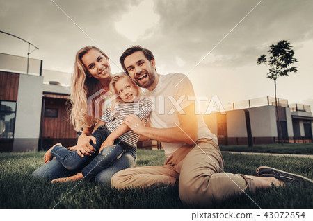 Smiling couple hugging cheerful child during sunset Smiling couple hugging cheerful child during sunset 43072854