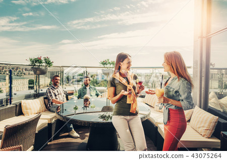 Beautiful young ladies with cocktails chatting while cheerful men sitting at the table Beautiful young ladies with cocktails chatting while cheerful men sitting at the table 43075264