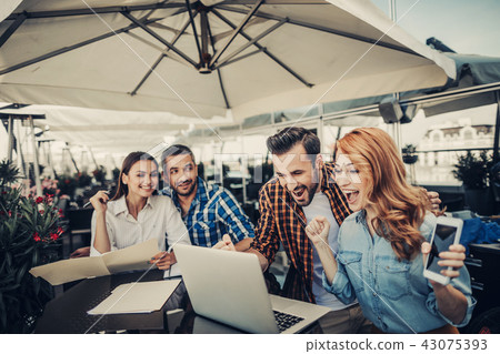 Young couple receiving good news online while smiling friends looking at them Young couple receiving good news online while smiling friends looking at them 43075393