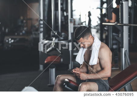 Serene ripped man is using smartphone during workout Serene ripped man is using smartphone during workout 43076095