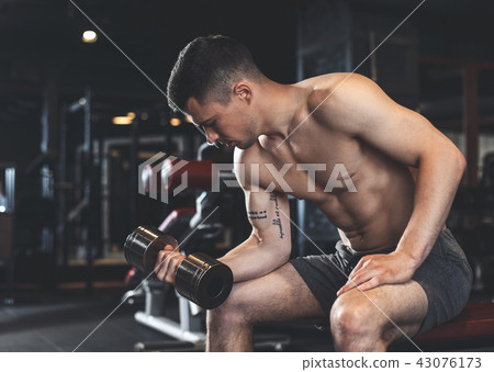 Concentrated man is training arms with weight 43076173