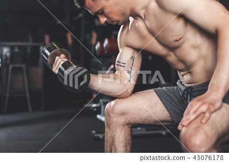 Ripped tattooed man is working on biceps relief Ripped tattooed man is working on biceps relief 43076178