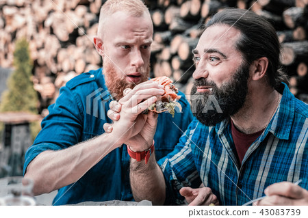 Bearded dark-haired man feeling amazing after biting some burger Bearded dark-haired man feeling amazing after biting some burger 43083739