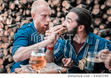 Hungry dark-haired man trying meat burger of his friend 43083740