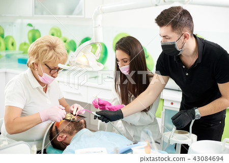 Dentist works with patient, she is assisted by two assistants Dentist works with patient, she is assisted by two assistants 43084694