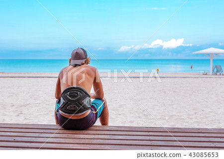 The surfer sits with his back to the camera on the terrace on the beach looking out into the 43085653