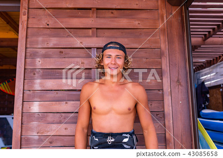 Young attceractive guy surfer standing on the terrace of a surf school looking at the camera Young attceractive guy surfer standing on the terrace of a surf school looking at the camera 43085658