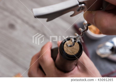 A hand opening a bottle of wine using an opener 43091265