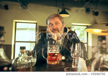 The sad senior bearded male drinking beer in pub 43098792