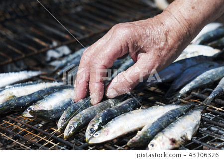 old woman salting some sardines in a grill old woman salting some sardines in a grill 43106326