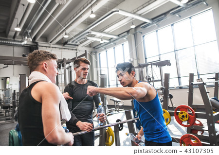 Young friends standing and talking in modern crossfit gym, holding plastic bottles. 43107305