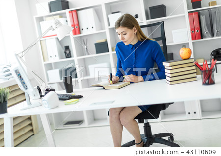 A young girl sits at a computer desk and holds a yellow marker in her hand. Before the girl lies an 43110609