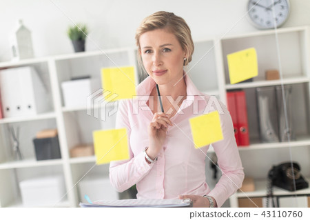 A young blonde girl stands in the office next to a transparent board with stickers and holds 43110760
