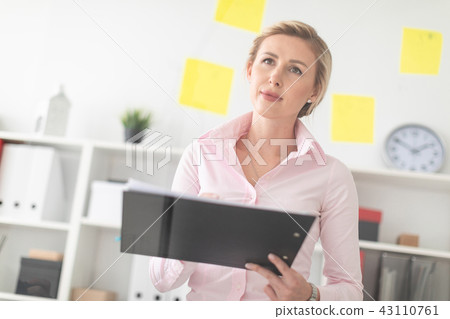A young blonde girl stands in the office next to a transparent board with stickers and holds 43110761