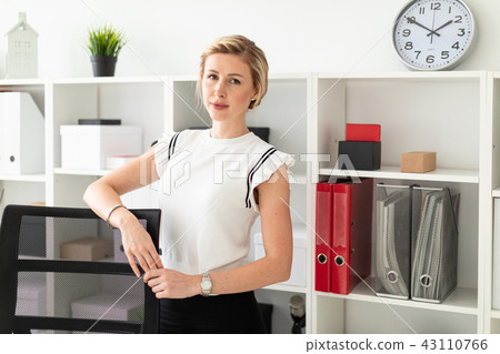 A young blonde girl stands in the office next to the shelving with documents, with her hands on the A young blonde girl stands in the office next to the shelving with documents, with her hands on the 43110766