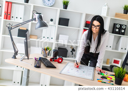 A young girl stands near a computer desk and draws a marker on a magnetic board. 43110814